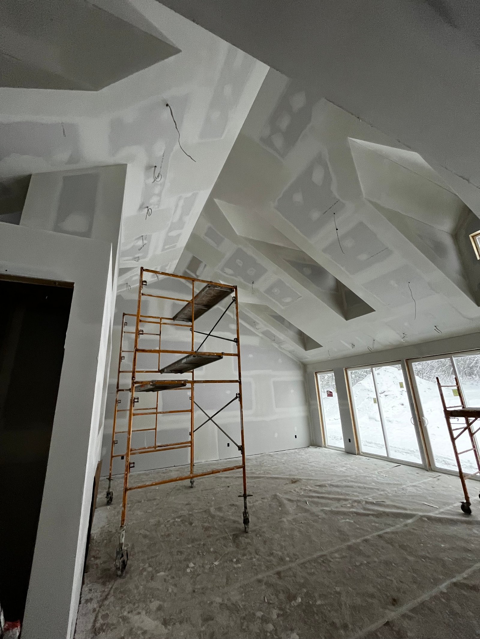 Interior construction site with metal scaffolding, drywall ceiling, and plastic sheeting