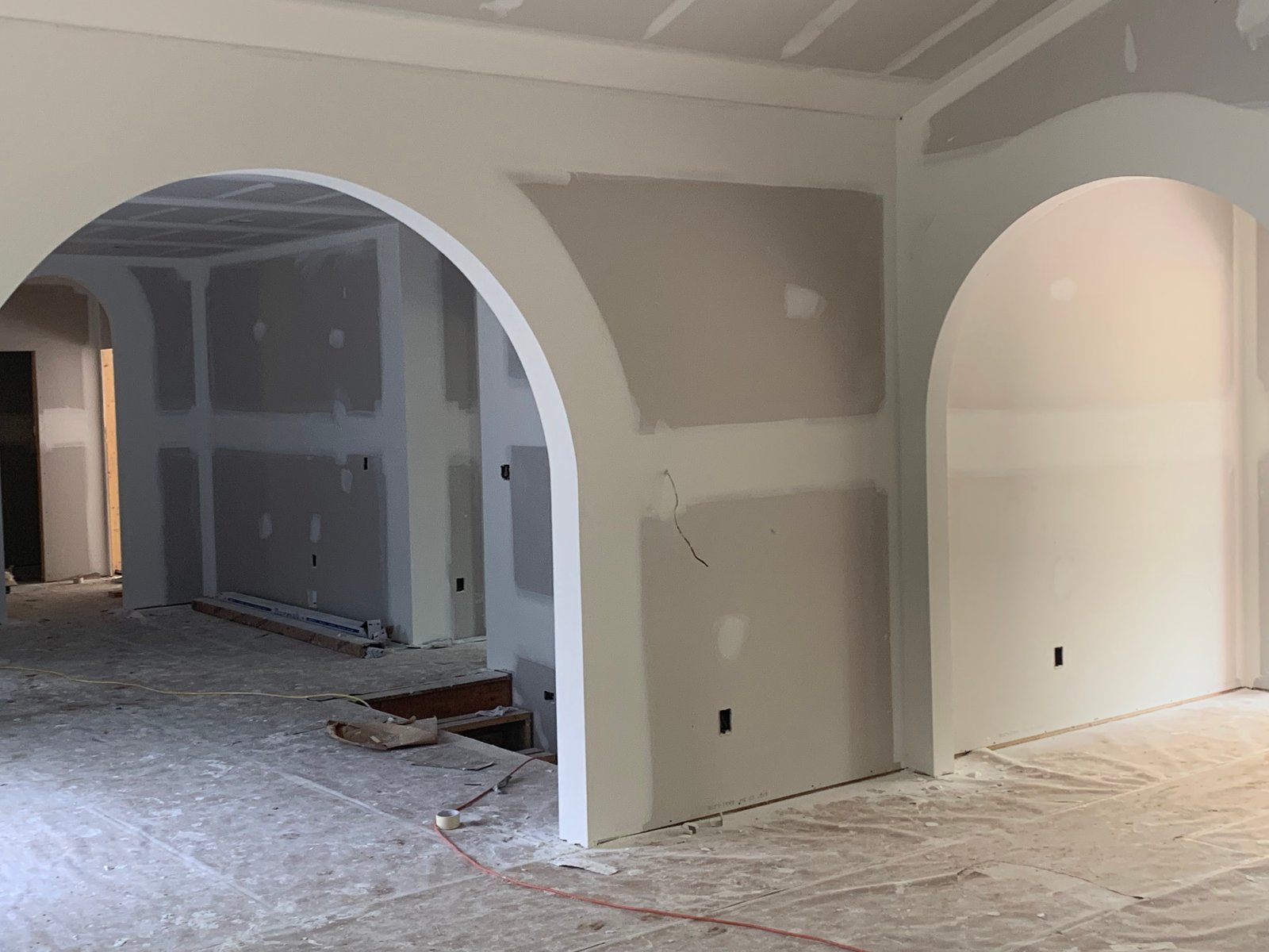 Interior construction site showing drywall installations with curved archway entrance, drywall sheets, and exposed studs